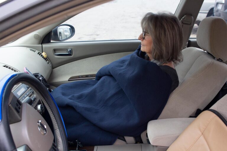 Woman in passenger seat covered with SubZero Heated Travel Blanket